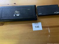 Two closed rectangular geometry set cases, one larger with Dedra branding, the other smaller with JPF Quimper branding, sitting on a wooden surface with a lot number card.