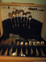 Full set of flatware displayed inside wood framed presentation case with fabric interior showing various spoons, forks and knives arranged in two rows