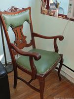 Full view of antique wooden armchair showing green faux leather upholstery on seat and back with carved wood arms and base