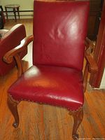 Front view of armchair showing red leather seat and backrest, carved wooden armrests and legs, with nailhead trim on seat edge.