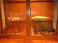 Wooden cabinet shelf with assorted glassware including clear bowls, plates, and platters displaying the variety and condition of items.