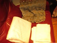 Four bed linen items: Bella Notte patterned blue-green Euro sham, two white cotton sateen Euro shams, and folded white duvet cover, displayed on a red surface.