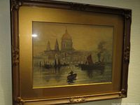 Framed watercolour painting showing a riverside scene with boats and a domed building under soft lighting, reflective glare on glass.