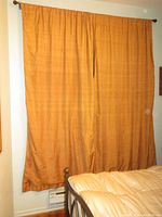 Two gold drape panels hanging fully cover a window, mounted on a pewter-colored metal extendable rod with decorative round finials. Panels have a slight sheen and appear lined.
