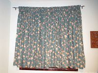 Full view of two cotton curtain panels hung on wall rod, dark teal with orange and cream floral pattern.