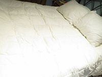Queen sized down duvet spread on bed with two pillows against headboard, showing quilted design and overall clean condition.