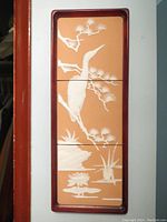 Full view of the three parian porcelain tiles mounted vertically in a solid hardwood frame colored dark brown. Relief shows a heron on tree branches with water elements in white on tan background.
