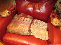 Two Benares silk shawls and pair of embroidered leather shoes placed on red leather chair; shawls show gold thread embroidery, pink shawl stained, shoes show embroidery with some fraying.