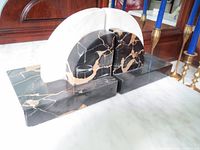 Pair of black marble with gold veining and white marble curved bookends on white surface, angled to show fronts and sides.