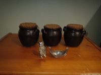 Full view of three black stoneware pots with cork lids, a silver-tone Viking figure, and a pewter salt cellar shaped like a Viking ship on a wooden surface.