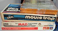 Stack of four vintage board games showing titles Mouse Trap, The Mad Magazine Game, and Scrabble Crossword Game for Juniors. The top game is wrapped in plastic. Boxes show signs of age and wear.