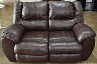 Front view of the dark brown leather loveseat recliner showing the two cushions, padded armrests, and stitching details.