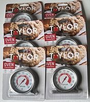 Six Taylor brand oven thermometers still in original packaging, each featuring a round dial thermometer measuring up to 600°F, packaged with an image of cookies baked in an oven.