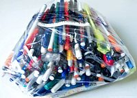 Plastic bag containing a large quantity of assorted used pens, pencils, markers, and highlighters, displayed from the front.