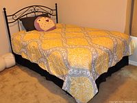Full size bed fully made with patterned bedding and decorative pillow; black metal headboard visible.