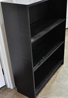 Photo of a black-brown Ikea BILLY bookcase showing three shelves and side panels; no visible damage, surface appears slightly worn.