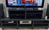 Image showing the black Ikea TV entertainment center with a television on top, two open compartments above, and shelves below including space for an audio receiver.