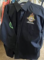 Front view of black button-down shirt showing skull and flames logo on chest and sleeve patch.