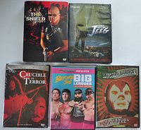 Top-down view of 5 sealed DVD cases arranged in two rows: The Shield Season 3, They Call Me Jeeg, Crucible of Terror, Before The Big Leagues, and Lucha Libre.