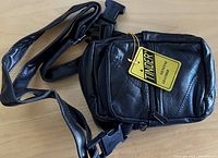 Front view of the black leather Tinder shoulder bag showing brand tag, zipper, and adjustable strap with buckle.