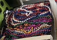 Tin box filled with many assorted colorful beaded necklaces and strands showing vibrant colors and different styles, some still with original tags.
