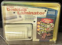 Photo showing vintage Aurora Desktop Laminator in its original sealed packaging with bonus lamination pouches included.