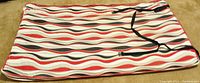 Zippered travel mattress cover showing colorful wavy stripe pattern in red, gray, black, and white, lying flat