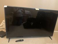 Front view of TV on floor with remote placed at center of screen base