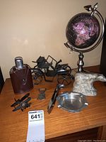 Photo showing all items together on a wooden surface: flask, globe, motorcycle model, polar bear carving, bottle opener, ashtray, and airplane figurines