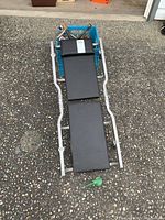 Full view of padded mechanic's creeper on asphalt surface showing the three cushioned segments and metal frame.