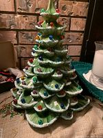 Front view of porcelain Christmas tree with colored bulbs attached to scalloped branches with white snow-like accents