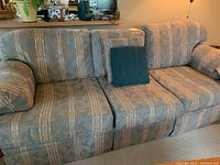 Side view of a three-seat sofa upholstered in gold and green patterned fabric with a green pillow on the left side.