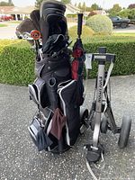 Golf bag filled with various golf clubs and an Evolution golf push cart beside it, showing the overall lot contents.