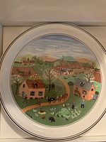 Round decorative plate illustrating a spring countryside village scene with houses, trees, animals, and people farming, part of Villeroy and Boch Four Seasons series.