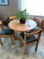 Round wooden kitchen table with four wooden chairs arranged around it, plant centerpiece on table.
