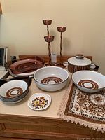 Wide shot of Stonehedge Midwinter ceramic dish set including bowls, plates, casserole dish, and copper candle holders on countertop.