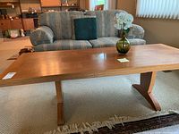 Wooden dining table in living room setting with a vase on top, showing overall design and structure of table including legs and surface pattern.