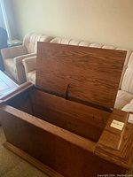 Wooden storage cabinet with its lid open, showing the interior storage space and wood grain details.