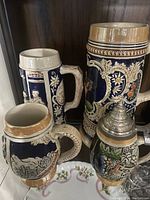 Four assorted German beer steins grouped together showing front and side details.