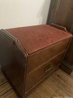 View of antique wooden bench with reddish padded seat, showing wood finish and bench shape.