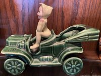 Side view of ceramic pixie elf seated on green ceramic vintage car, showing detail of figure and car sides.