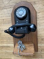 Front view of the antique black Bakelite rotary dial telephone mounted on wood backboard.