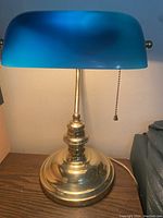 Full view of the banker’s lamp showing the brass base and blue glass shade from front angle with lamp on.