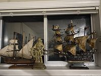 Photo showing the brass captain figurine between two model ships with sails in window background.