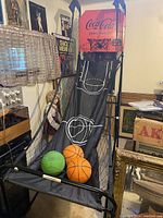 Photo showing Coca Cola branded basketball arcade game with net sides, 2 orange basketballs, and one green ball on the ramp.
