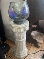 Front view of the off-white terracotta column plant stand supporting a glass bowl with artificial plants.