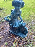 Photo of the garden ornament planter showing a girl figurine holding a watering can with integrated planter basket on base, made of plastic or resin, placed on grass.