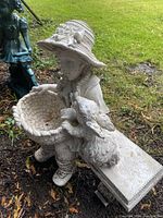 Side angle photo of the garden ornament showing the girl holding a basket and the dog figure on a bench.