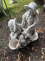 Photo showing the side angle of the boy and girl statue, highlighting the bucket planter and hats on each figure.