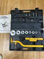 Full view of the metal bender kit showing yellow bending arms, circular bending dies, bolts, rods, and instruction manual inside a black plastic case.